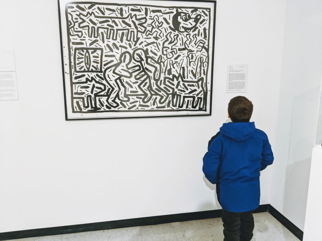 Kid standing in front of Keith Haring painting